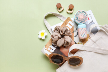 Bag with female summer accessories, fashion magazines and mini fan on green background