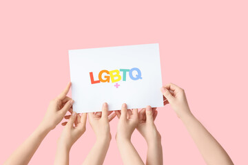 Female hands holding paper with abbreviation LGBTQ+ on pink background