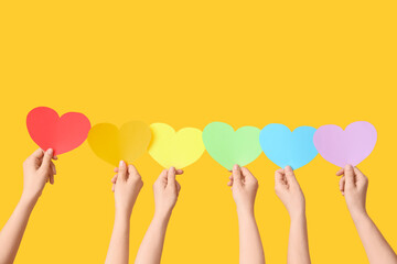 Female hands with colorful hearts on yellow background. LGBT concept