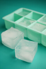 Ice cubes and tray on teal surface with two cubes separated