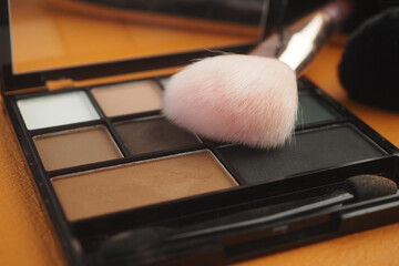 Makeup palette with brushes on wooden surface in soft light
