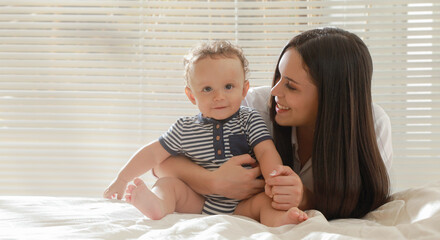 Young mother and baby smiling on a bed in a space illuminated by natural light.