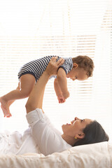 Mother playing with her baby on the bed in a bright home interior