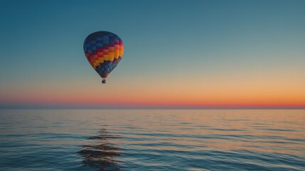 Colorful hot air balloon floats above calm ocean at sunrise.
