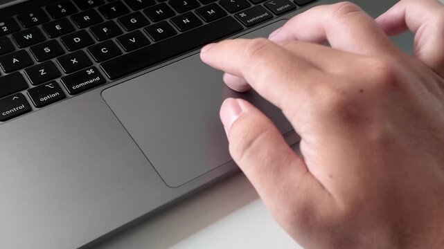 Side view close up of a hand swiping on a touch pad on a laptop on a white table. Working in a office. Working remotely