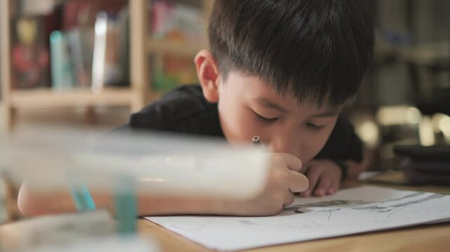 Asian boy about 7 years old drawing picture by pencil on white paper