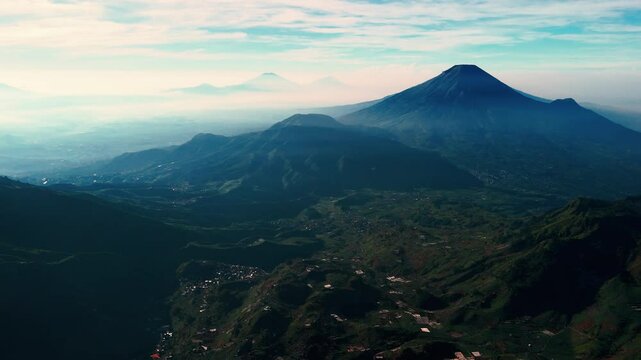 Aerial views of Mount Sindoro and Mount Sumbing in the distance from peak of Mount Prau, Dieng, Wonosobo, Indonesia with soft mist on the mountain slopes at dawn.
