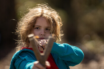 Portrait of a little shooter aiming. Dangerous childhood mischief. Kids game with a slingshot. Kids...