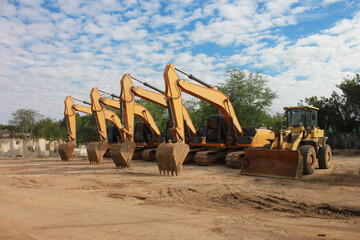 Lots of excavators parked on construction area of industrial building in construction site under the blue sky background.Earthmoving construction equipment