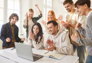 Happy young team looking at laptop screen, celebrating success in office or classroom. Excited...