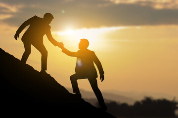 Businessman Helping Partner Climb a Hill at Sunrise