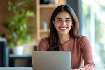 Smiling young woman using a laptop in a well-lit office space with plants in the background.