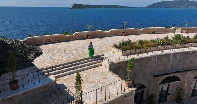 Close drone circling woman walking along overlook of Mamula Island fortress walls and inner courtyard from above