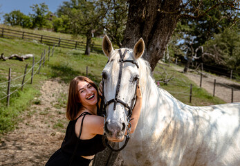 Obraz premium Smiling young caucasian female embraces white horse outdoors