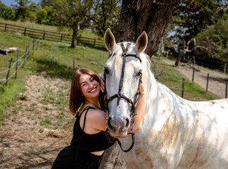 Young caucasian female embracing horse in sunlit pasture