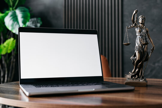 Lawyer's office. Statue of justice with scales and a white screen laptop in a modern office cubicle. Layout for advertising. Concept of legal law.