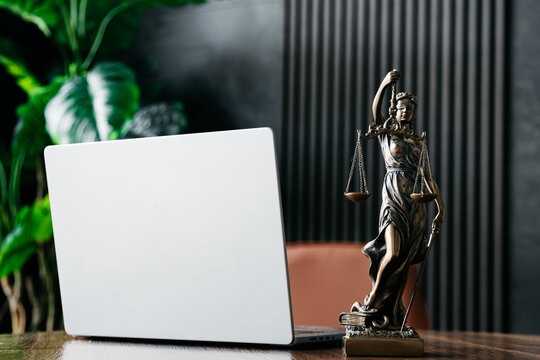 Lawyer's office. Statue of justice with scales and a laptop in a modern office cubicle. Concept of legal law, counseling and concept of justice.