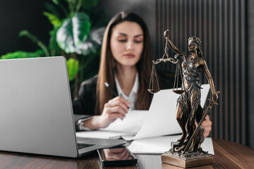 A female lawyer works on a laptop with scales of justice on a courtroom table. Law and legal...