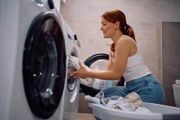 Happy woman loading laundry in washing machine.
