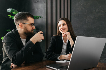  Two business team leaders man and woman working in the office at a corporate meeting at a laptop in the lobby of a modern office. Business concept. 