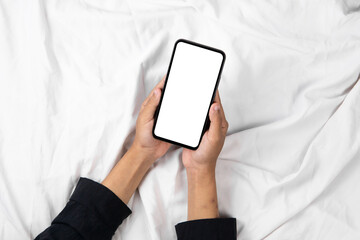 Hand holding smartphone with blank white screen on bed