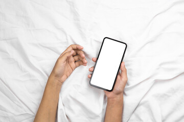Hand holding smartphone with blank white screen on bed