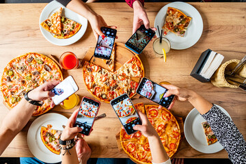 Handheld devices snap pictures as friends enjoy sharing pizza and drinks together at a restaurant