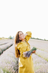 woman in yellow dress stands in lavender field, gently holding bouquet of lavender flowers. She appears serene and contemplative, enjoying beauty and fragrance of blossoms around her.
