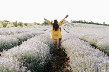 woman in yellow dress stands in lavender field, gently holding bouquet of lavender flowers. She appears serene and contemplative, enjoying beauty and fragrance of blossoms around her.