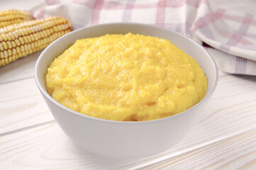 Delicious corn porridge in a bowl on a white wooden table.