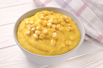 Delicious corn porridge in a bowl on a white wooden table.