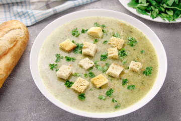 Homemade cream soup with chicken and herbs in a white plate on a gray background.