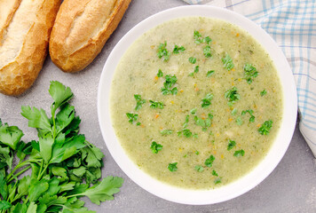 Homemade cream soup with chicken and herbs in a white plate on a gray background.