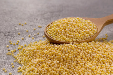 Millet grains in wooden spoon on a gray background