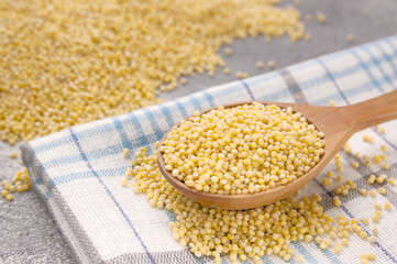 Millet grains in wooden spoon on a gray background