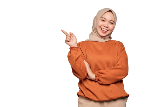 Cheerful young Asian woman in orange shirt pointing fingers at copy space isolated on transparent background