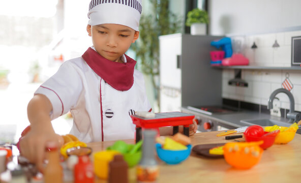 Little boy in chef hat and apron cooking in toy kitchen. Educational toys for young children. Kids play, portrait of Cute little Asian.playing at kitchen at indoor playground
