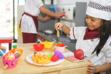 two little cute funny smiling kids wearing a white chef's hats and uniform decorating easter bread with food coloring in the grey and white kitchen with easter decorations