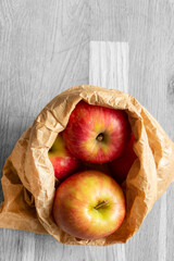 Apples in a brown paper bag on a wood background with selective colour.  Environmentally friendly packaging concept