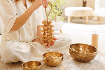 Hands holding a seed rattle during meditation session with singing bowls on carpeted floor.