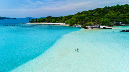 Crystal-clear water meets soft white sand at Koh Kham, Thailand. Vibrant tropical foliage frames...