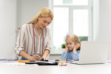 Fototapeta premium Mother tailoring a new model in her dress design studio, her daughter watching