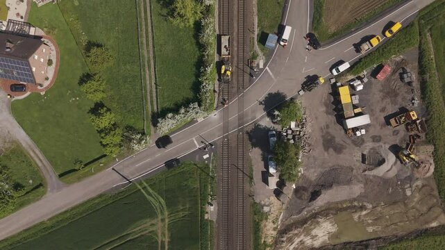 Top-down drone shot of a construction site at a railway crossing in Unna, Germany. Roadworks and vehicles near railway tracks on a sunny spring day.