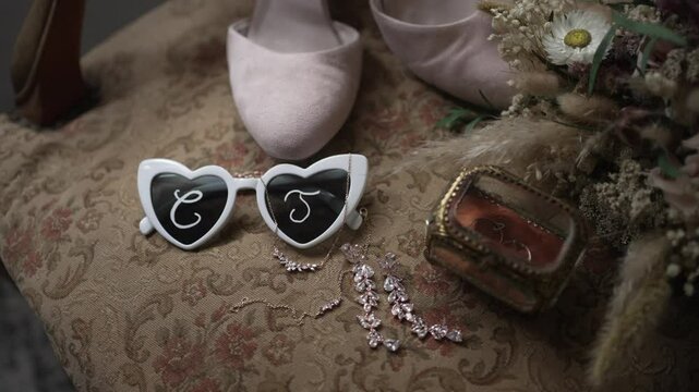 Close up of heart shaped sunglasses with initials beside wedding shoes and bridal jewelry