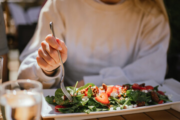 Close up of young woman eating fresh strawberry salad at outdoor table