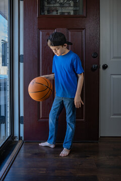 boy in casual wear bouncing basketball on wood floor by front door
