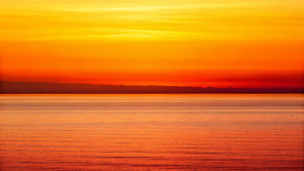 Fototapeta premium Vibrant Sunset Over Calm Ocean Waves with Beautiful Orange and Yellow Sky Colors