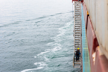 A deckhand prepares the pilot ladder as the ship readies for port entry. Secured in a safety...