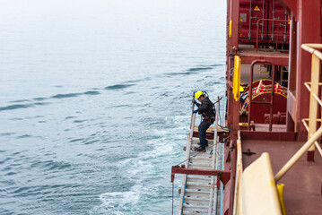 A deckhand prepares the pilot ladder as the ship readies for port entry. Secured in a safety...