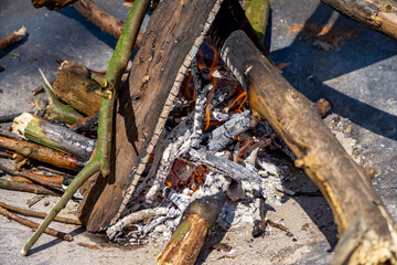 close-up view of a campfire with stacked wooden logs, glowing embers, and visible ash. The rustic...